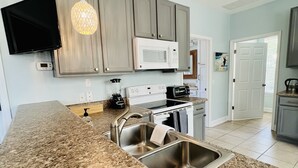 A modern kitchen with granite countertops, stainless steel sinks, a microwave, stove, and a hanging light fixture. -  Bayside Cottage 4 miles to Destin, Shopping & Beaches, minutes to Elgin AFB (Niceville)