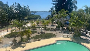 A swimming pool with a curved edge, surrounded by palm trees and a view of a body of water. - Luxury Bayview Wellness Retreat w/Pool, Salt-Water Jacuzzi, Hot Tub...+ more! (Bradenton)
