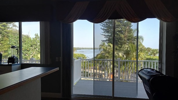 A room with a large sliding glass door leading to a balcony with a view of a lake and trees. - Luxury Bayview Wellness Retreat w/Pool, Salt-Water Jacuzzi, Hot Tub...+ more! (Bradenton)