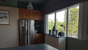 A kitchen with a stainless steel refrigerator, wooden cabinets, a large window with a view of trees, and a countertop with a blender. - Luxury Bayview Wellness Retreat w/Pool, Salt-Water Jacuzzi, Hot Tub...+ more! (Bradenton)