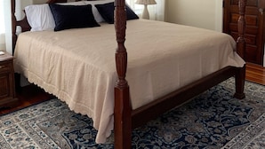 A four-poster bed with a wooden frame, a large floral painting on the wall, and a chandelier. - Historical Natchitoches Home, close to downtown and Cane River. (Natchitoches)