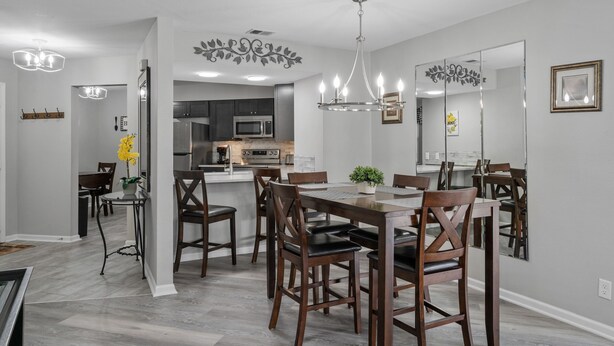 A modern dining area with a wooden table and chairs, a chandelier, and a large mirror on the wall. - Deluxe Golf Condo with Private, Covered Balcony - BEAUTIFUL View of the Ozarks (Branson)