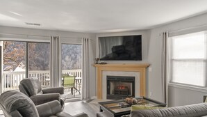A living room with a fireplace, leather chairs, a coffee table, and a large TV. - Deluxe Golf Condo with Private, Covered Balcony - BEAUTIFUL View of the Ozarks (Branson)