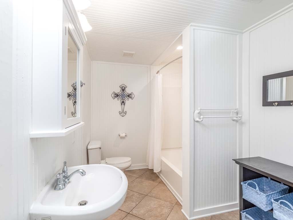 A bathroom with a white sink, toilet, and shower. There is a mirror above the sink and a towel rack on the wall.