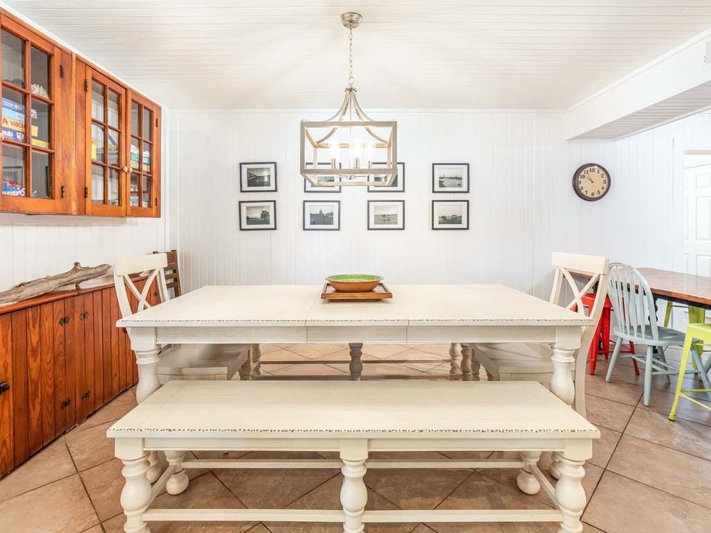 Un coin repas avec une table et des bancs blancs, des meubles en bois et un lustre.