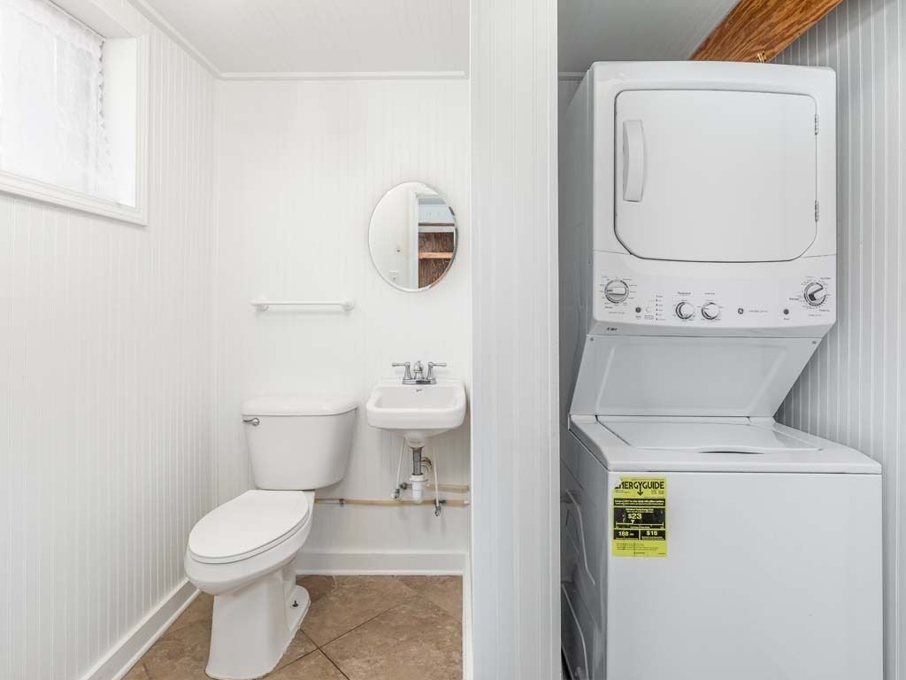 Ein kleines, weißes Badezimmer mit Toilette, Waschbecken und einem übereinander gestapelten Wasch- und Trocknerpaar.