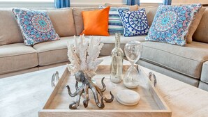 Un plateau en bois, orné d’objets décoratifs, est posé sur une table en marbre dans un salon où se trouve un canapé beige et des coussins à motifs.