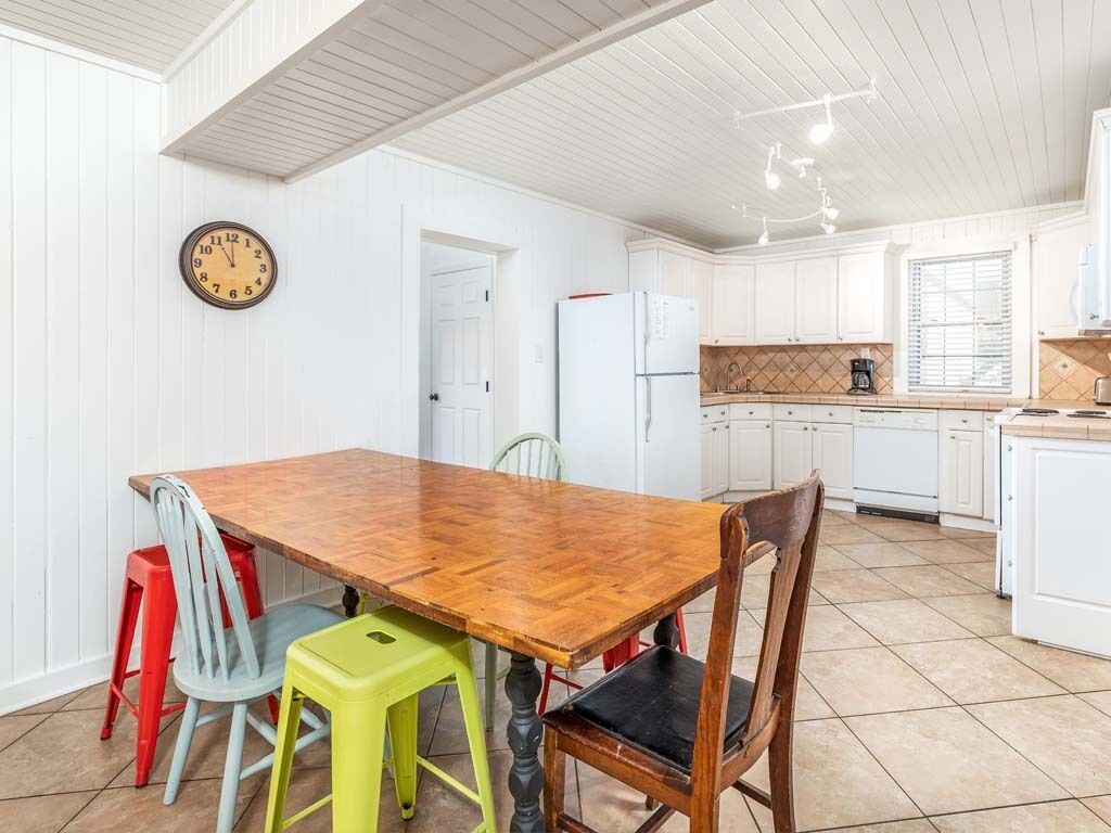 A kitchen with a wooden table, chairs, a clock, and white cabinets.