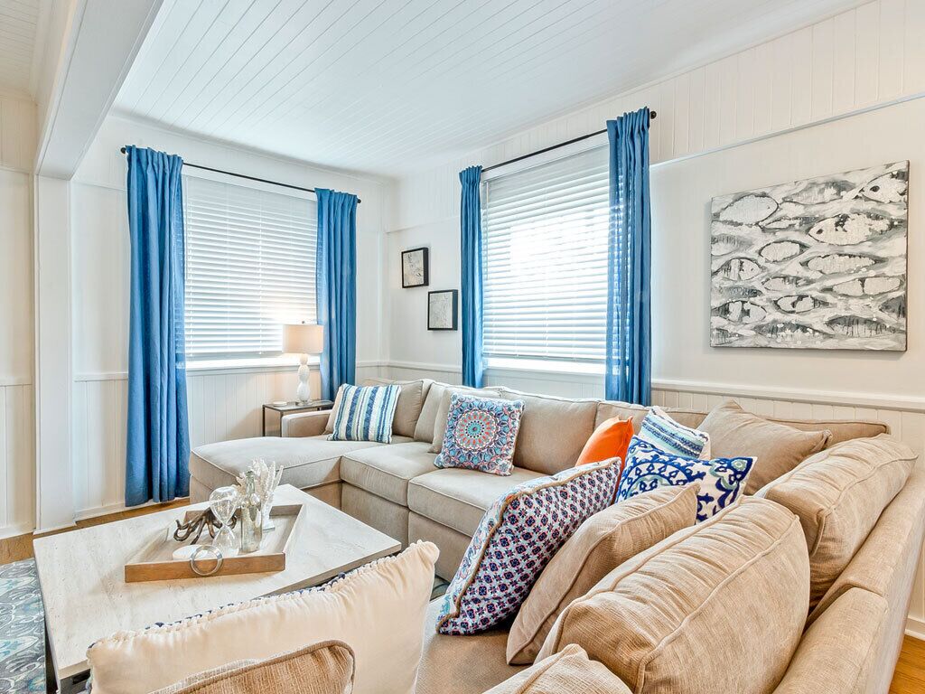 Una sala de estar con un sofá beige, cortinas azules y un cuadro en la pared.