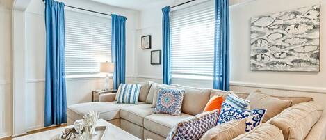 Una sala de estar con un sofá beige, cortinas azules y un cuadro en la pared.