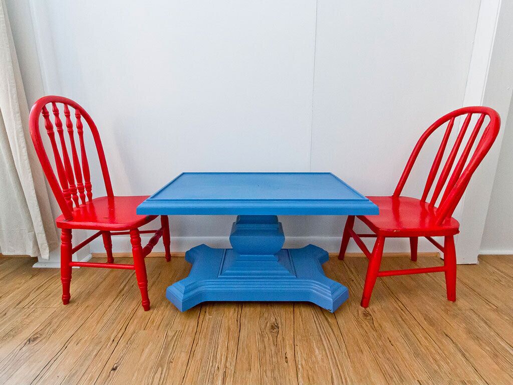 Une table bleue avec quatre chaises rouges, placée dans un coin.
