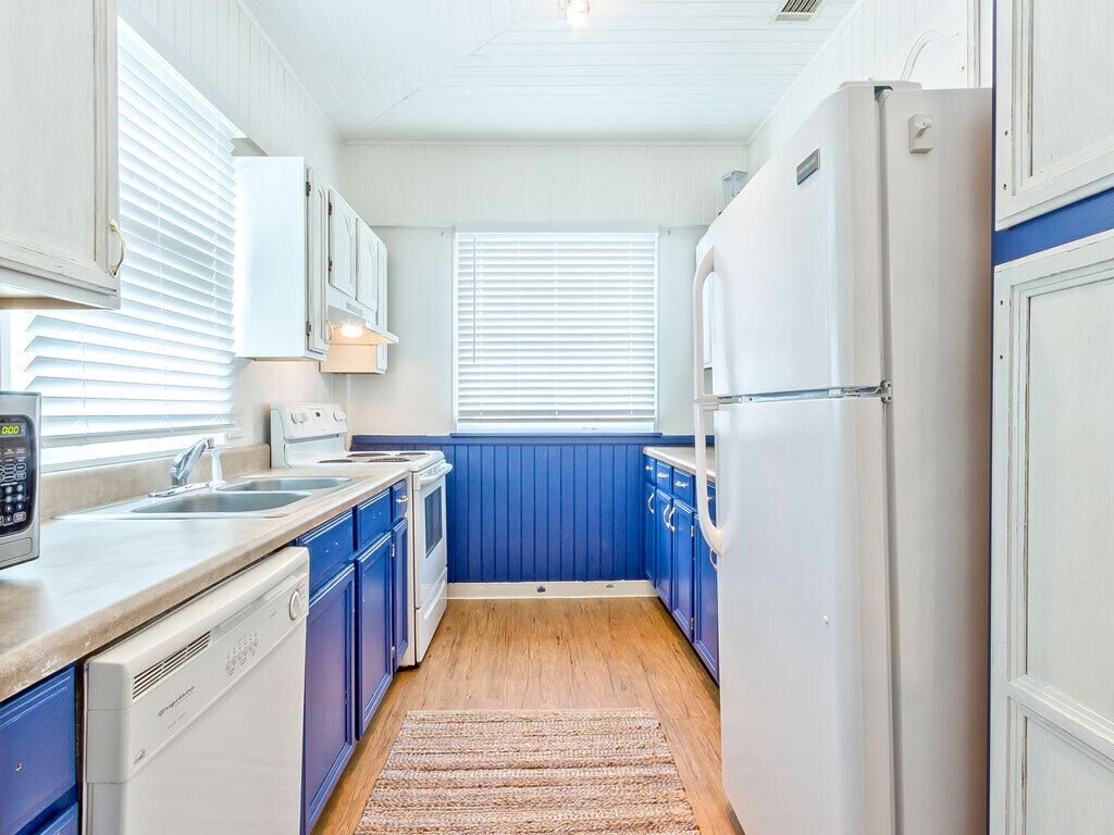 A compact kitchen with white appliances, blue cabinets, and a wooden floor.