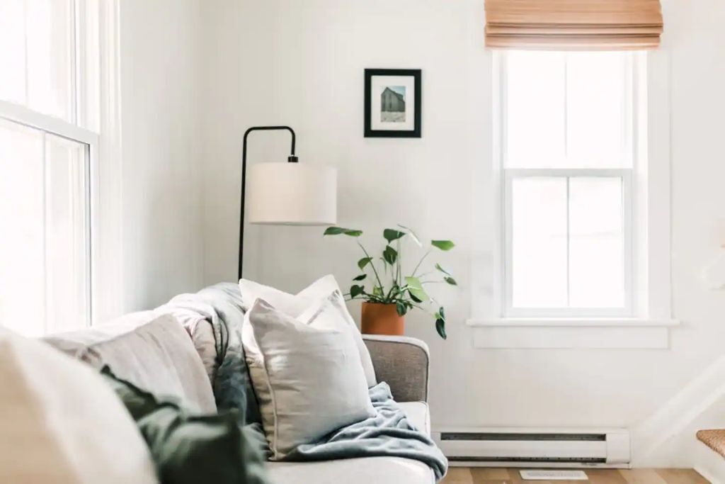 Un salon confortable avec un canapé, une lampe sur pied, une plante en pot et une fenêtre avec des stores.