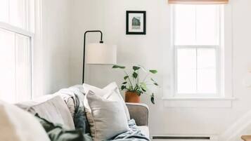 Un salon confortable avec un canapé, une lampe sur pied, une plante en pot et une fenêtre avec des stores.