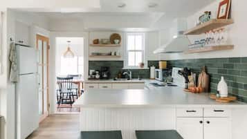 Une cuisine moderne avec des meubles blancs, un îlot central et des étagères en bois au-dessus du plan de travail.
