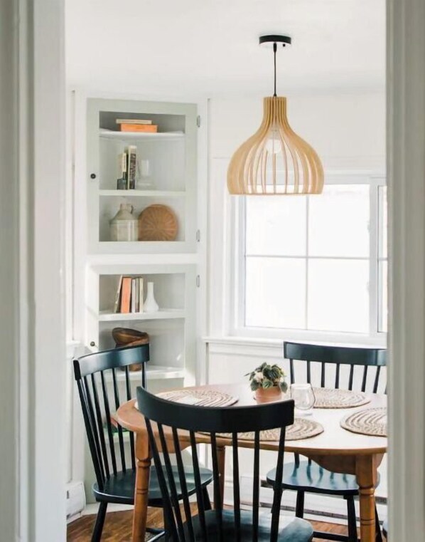 A dining area with a white interior, a wooden dining table with black chairs, and a hanging pendant light.
