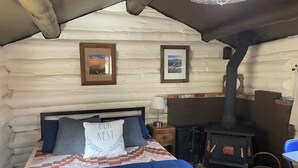 Um quarto de cabana de tronco aconchegante, com cama, colcha, travesseiro com a inscrição "OUR NEST" e lareira, além de quadros nas paredes.