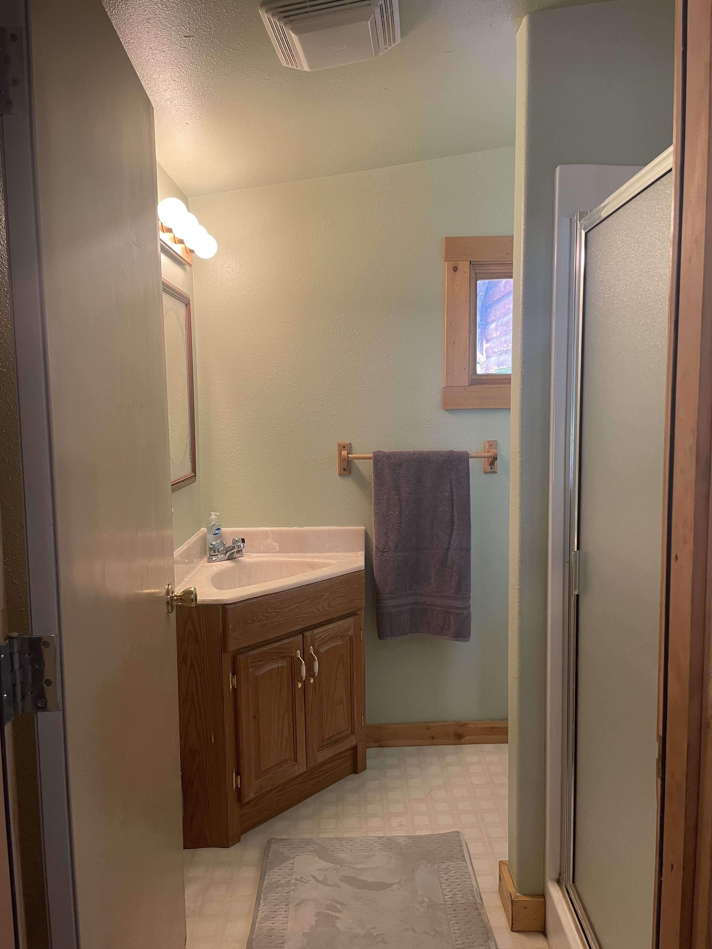 A bathroom with a wooden vanity, a sink, a mirror, a towel rack, and a window.