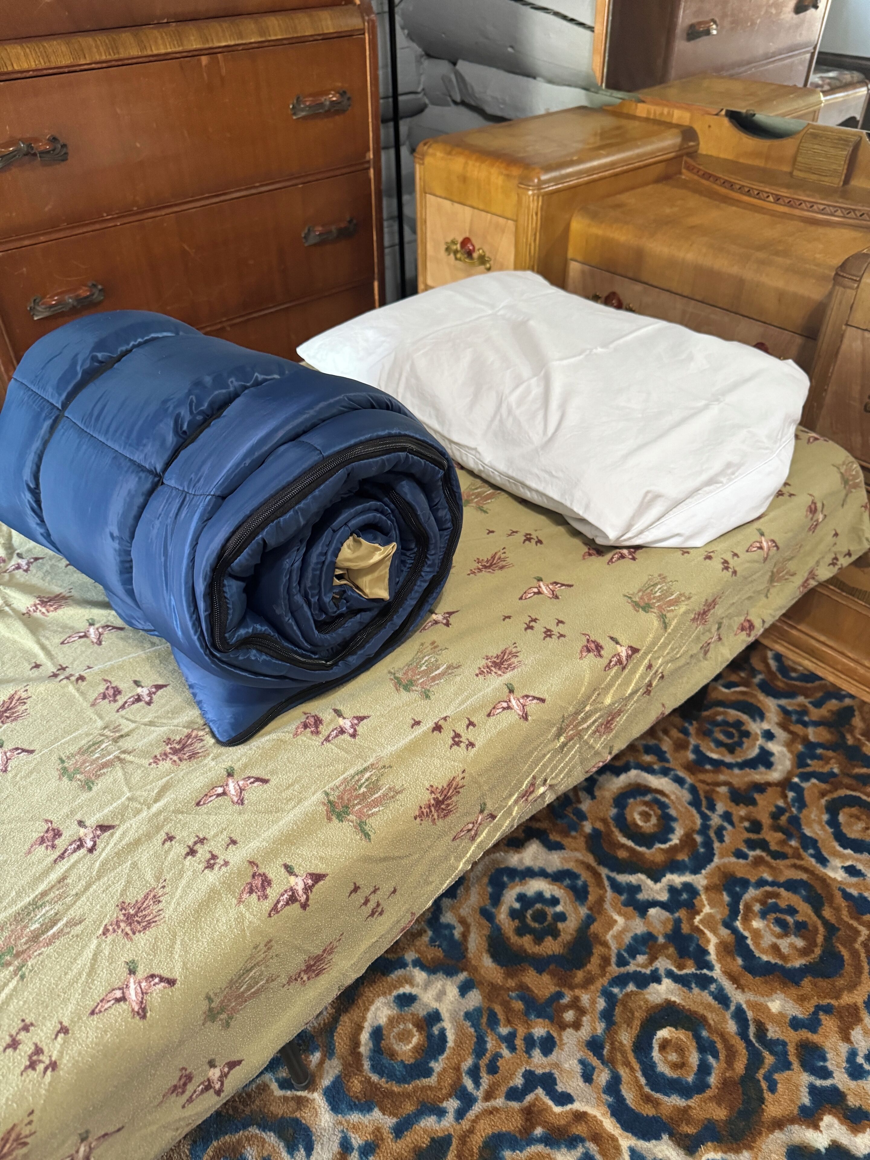 Un lit avec une couvre-lit à motifs floraux, une couverture bleue roulée et un oreiller blanc.