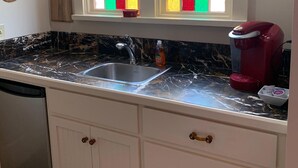 A kitchen with a double sink, a coffee maker, and a window with colorful stained glass.