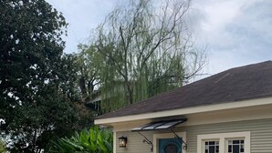 A single-story house with a front porch, a blue door, and a small garden area with plants and a tree.