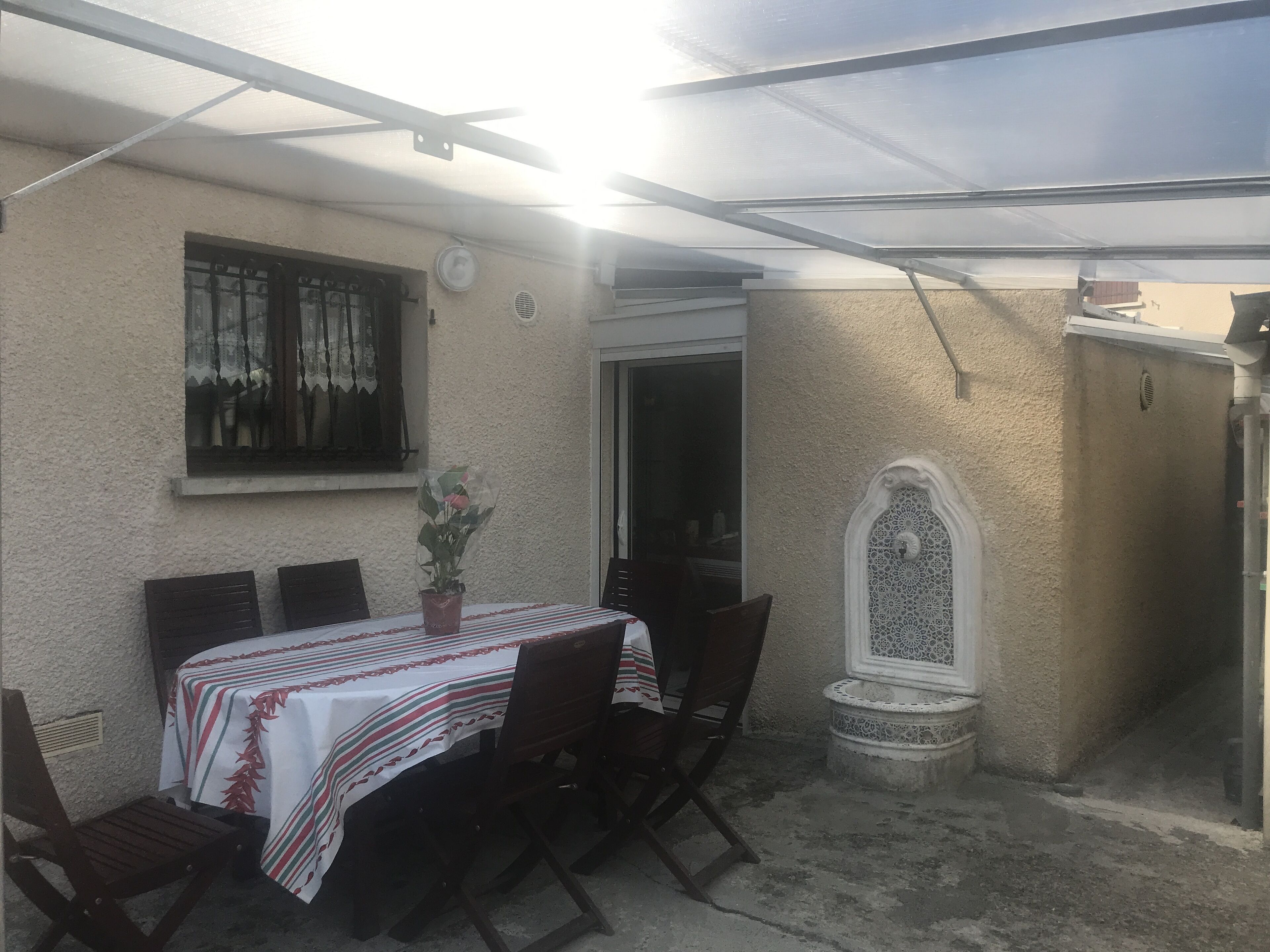 Une terrasse extérieure avec une table et des chaises, un pot de fleurs et un élément décoratif mural.