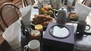 Una mesa de comedor con diversas opciones para el desayuno, incluyendo cruasanes, frutas y una tetera.
