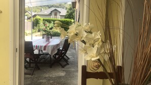 Un umbral abierto que da a un patio con una mesa y sillas, rodeado de vegetación y una casa al fondo.