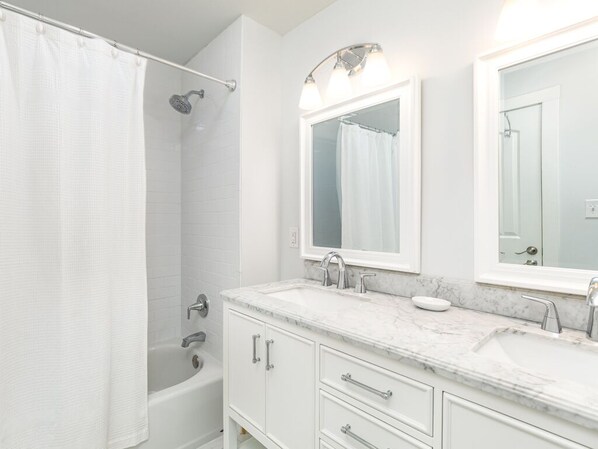 A bathroom with a bathtub, a double sink vanity, and a large mirror. - Blue Belle by Tybee Vacation Rentals (Tybee Island)