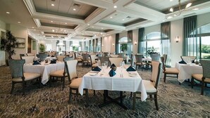 Un comedor amplio con varias mesas y sillas, ventanas grandes y suelo alfombrado.