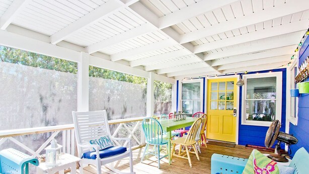 Un espacio al aire libre techado con un piso de madera, una puerta amarilla y una pared azul.