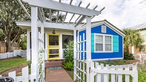 Una casa con fachada azul, un porche blanco y una puerta amarilla.