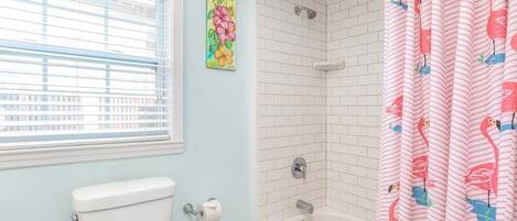 A bathroom with a toilet, a shower with white tiles, and a window with blinds.