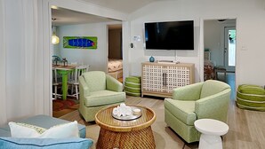 Una sala de estar moderna con sillones verdes, una mesa de centro redonda y un televisor de pantalla plana.