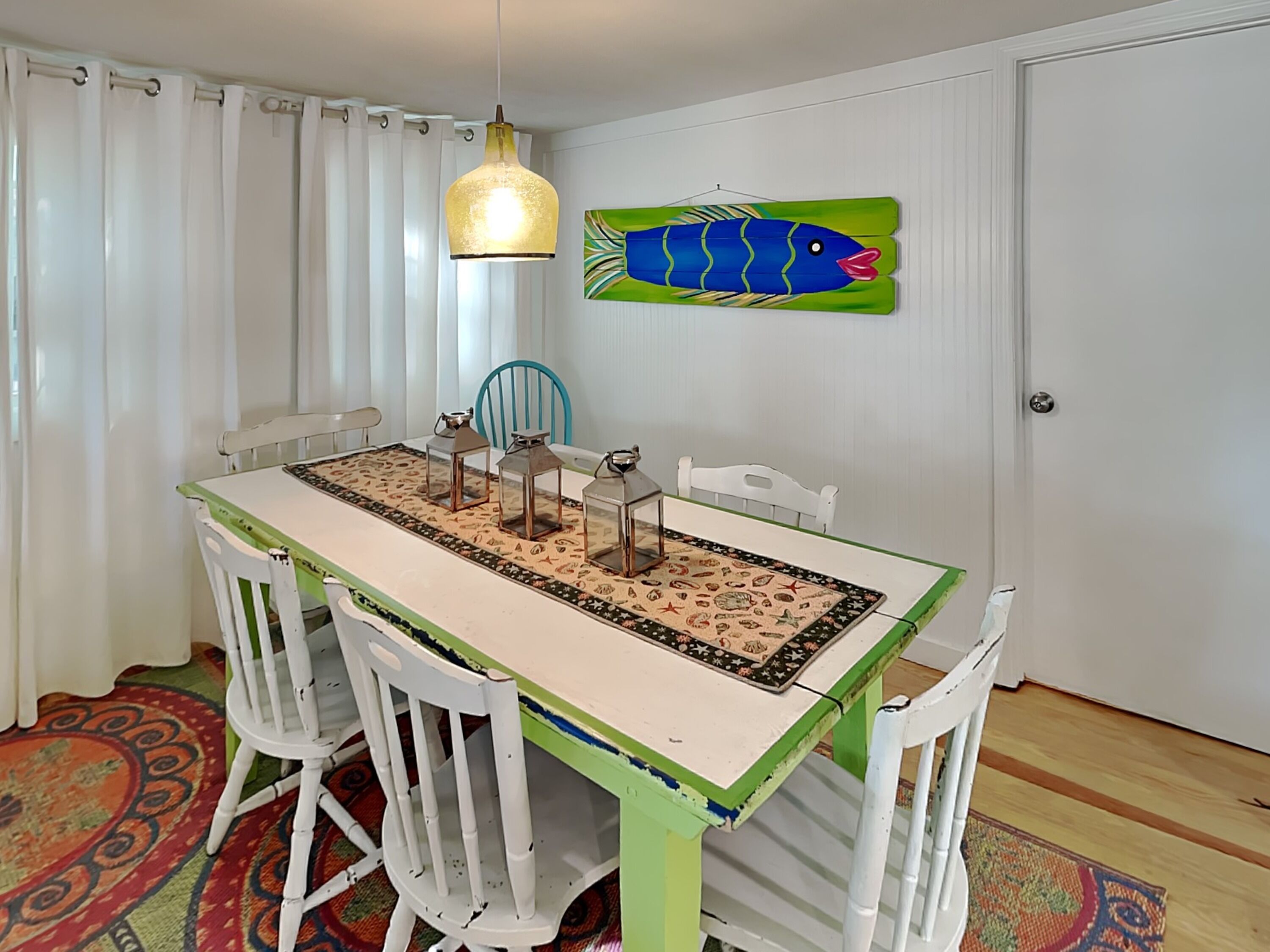 Un coin repas comprenant une table, des chaises, un luminaire suspendu et un décor mural représentant des poissons.