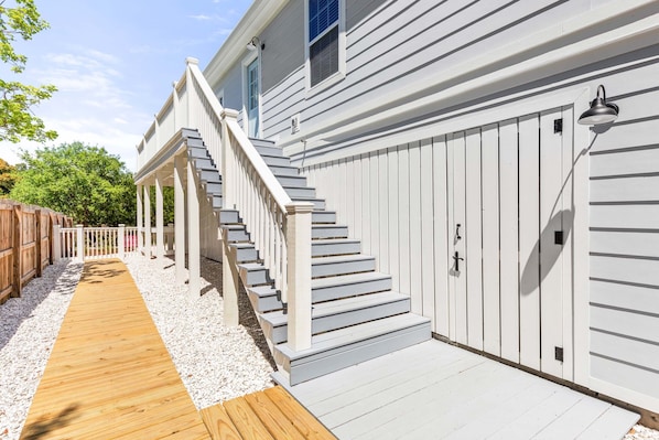 Staircase leads to a covered porch with a wooden deck and a gravel pathway.