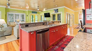 A modern kitchen with red cabinetry, granite countertops, and stainless steel appliances. - Blue Skies by Tybee Vacation Rentals (Tybee Island)