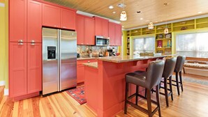 A modern kitchen with red cabinets, stainless steel appliances, and a wooden ceiling. - Blue Skies by Tybee Vacation Rentals (Tybee Island)
