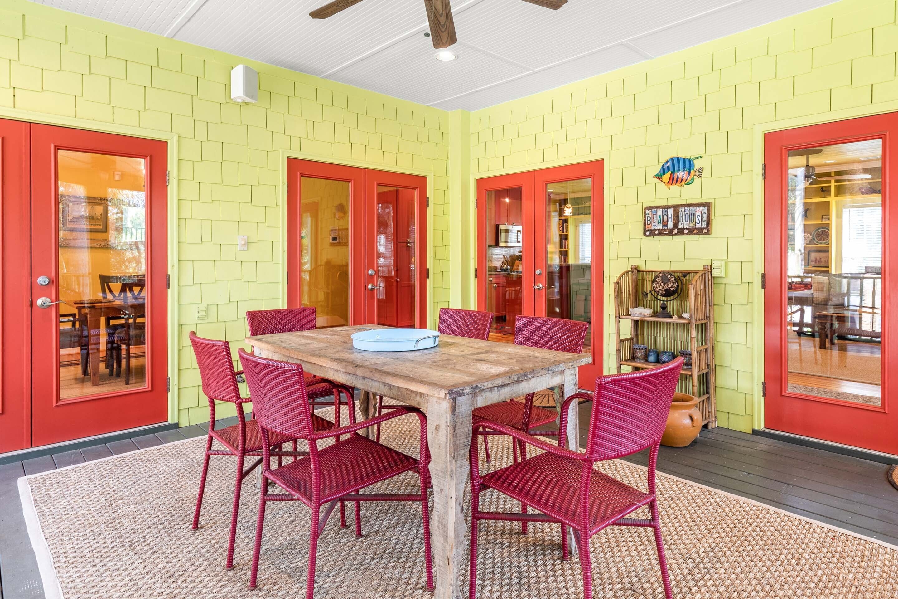 A dining area with a wooden table and red wicker chairs, surrounded by yellow brick walls and red doors.