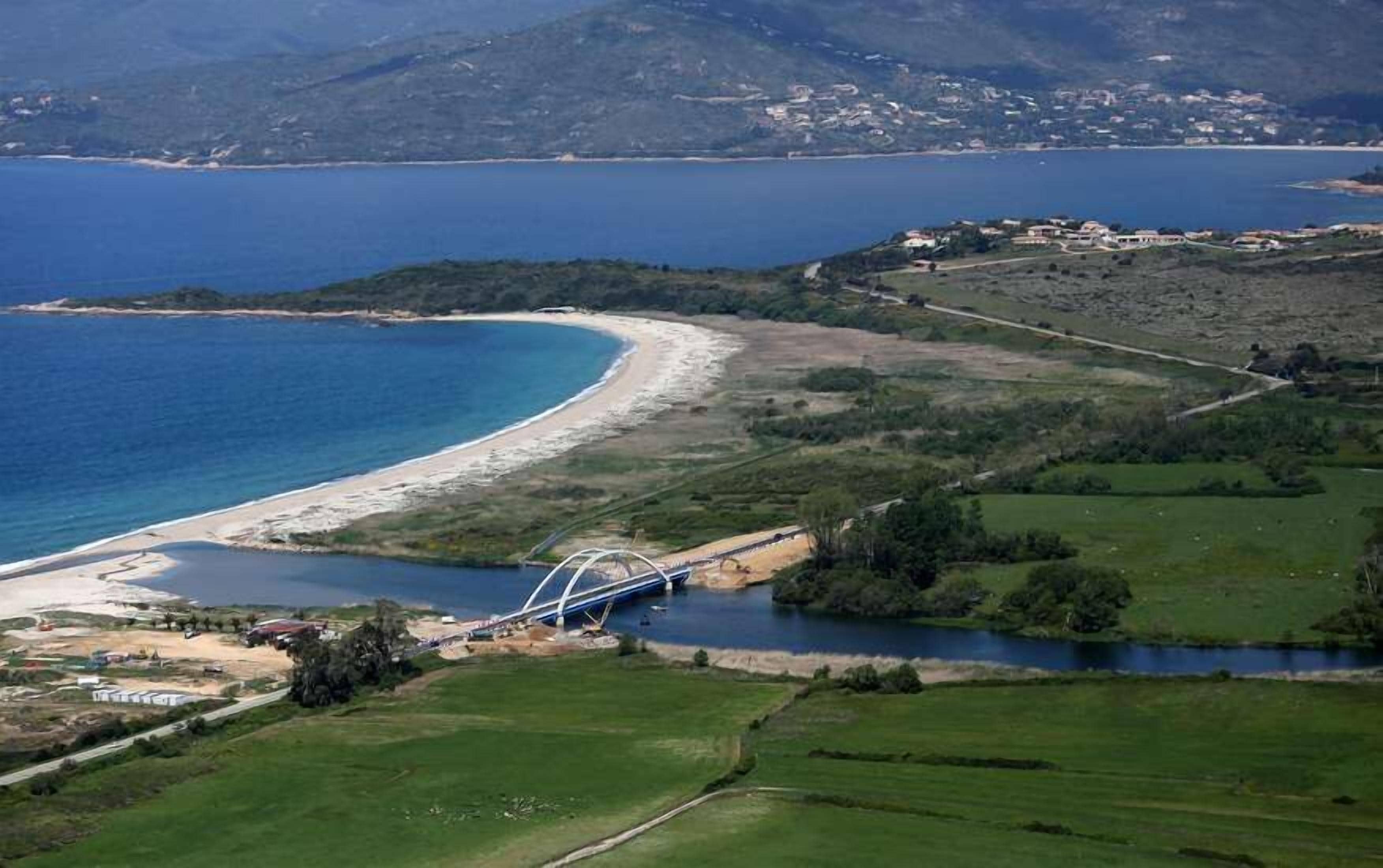 A coastal landscape with a bridge over a river, a beach, and a distant town.