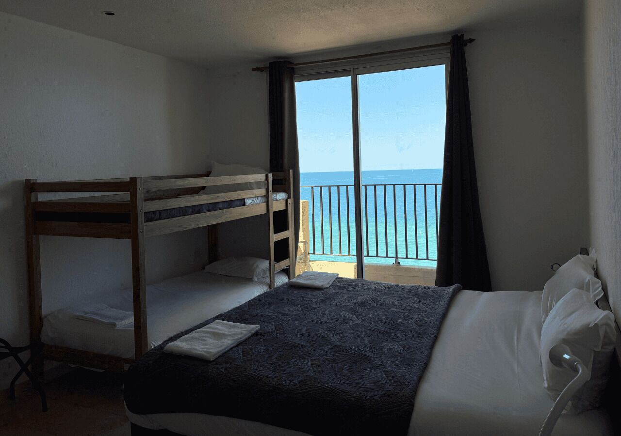 A room with a bunk bed, a single bed, and a view of the sea through a balcony.