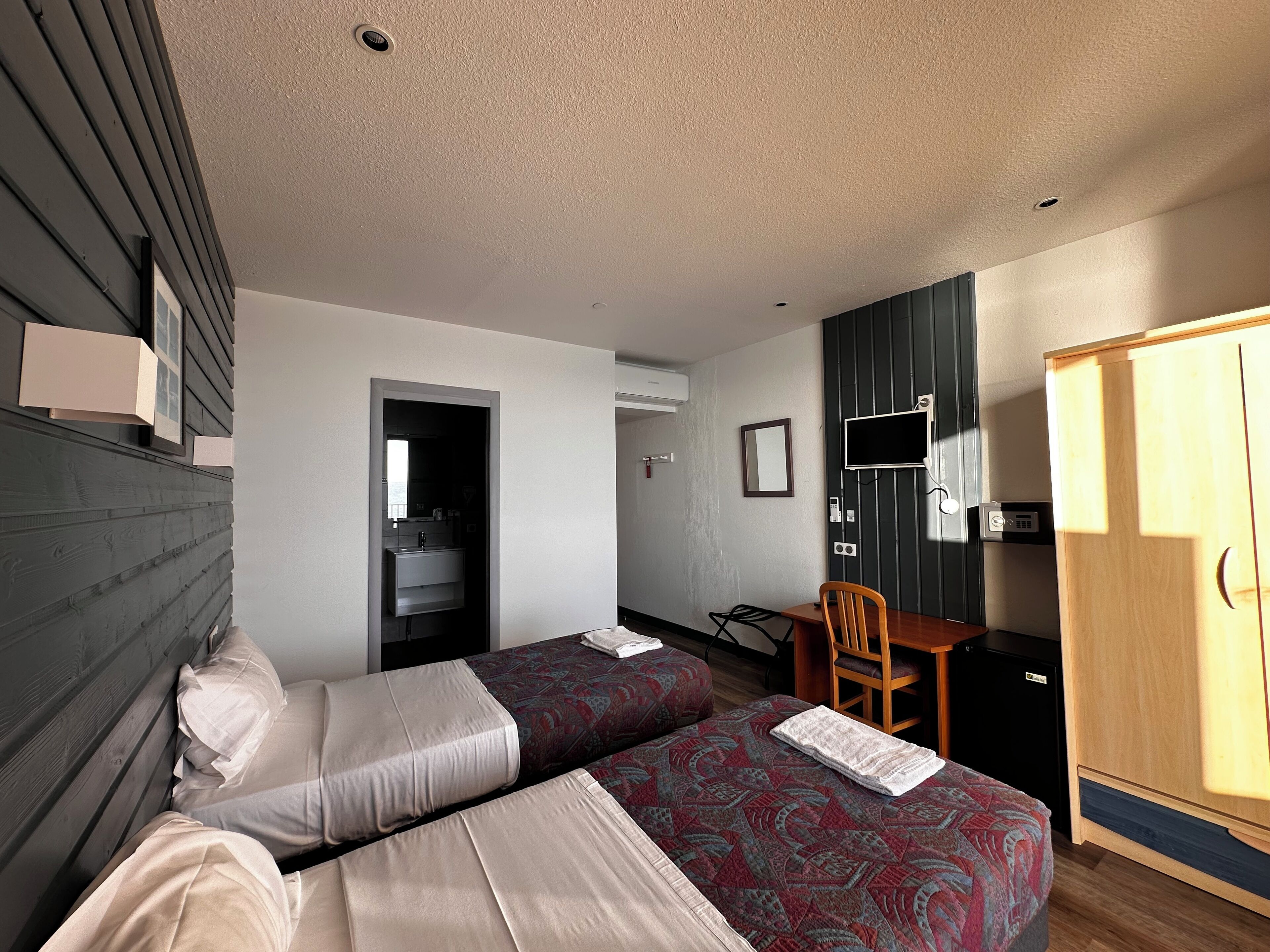 Habitación de hotel con dos camas, un escritorio, una silla, un armario y una televisión.