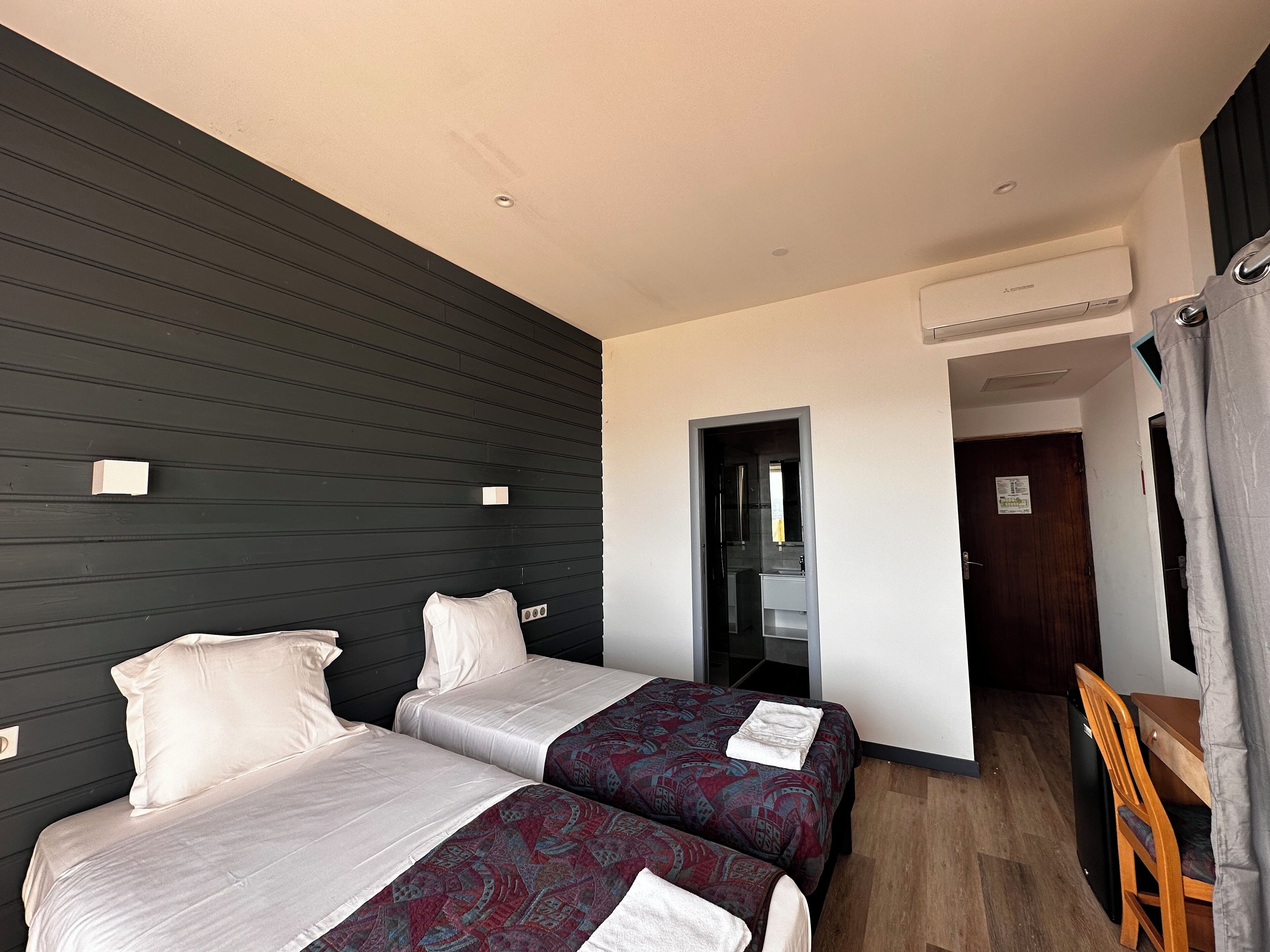 A hotel room with two beds, a desk, a chair, and an air conditioning unit.