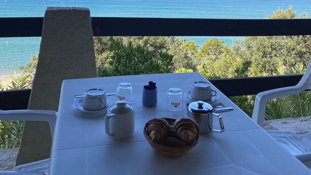 Una mesa con tetera y cruasanes, con vistas a la costa.