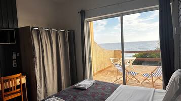 Habitación de hotel con cama, televisor, escritorio y balcón con vista al mar.