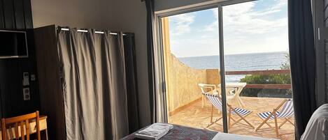 A hotel room with a bed, a TV, a desk, and a balcony with a view of the sea.