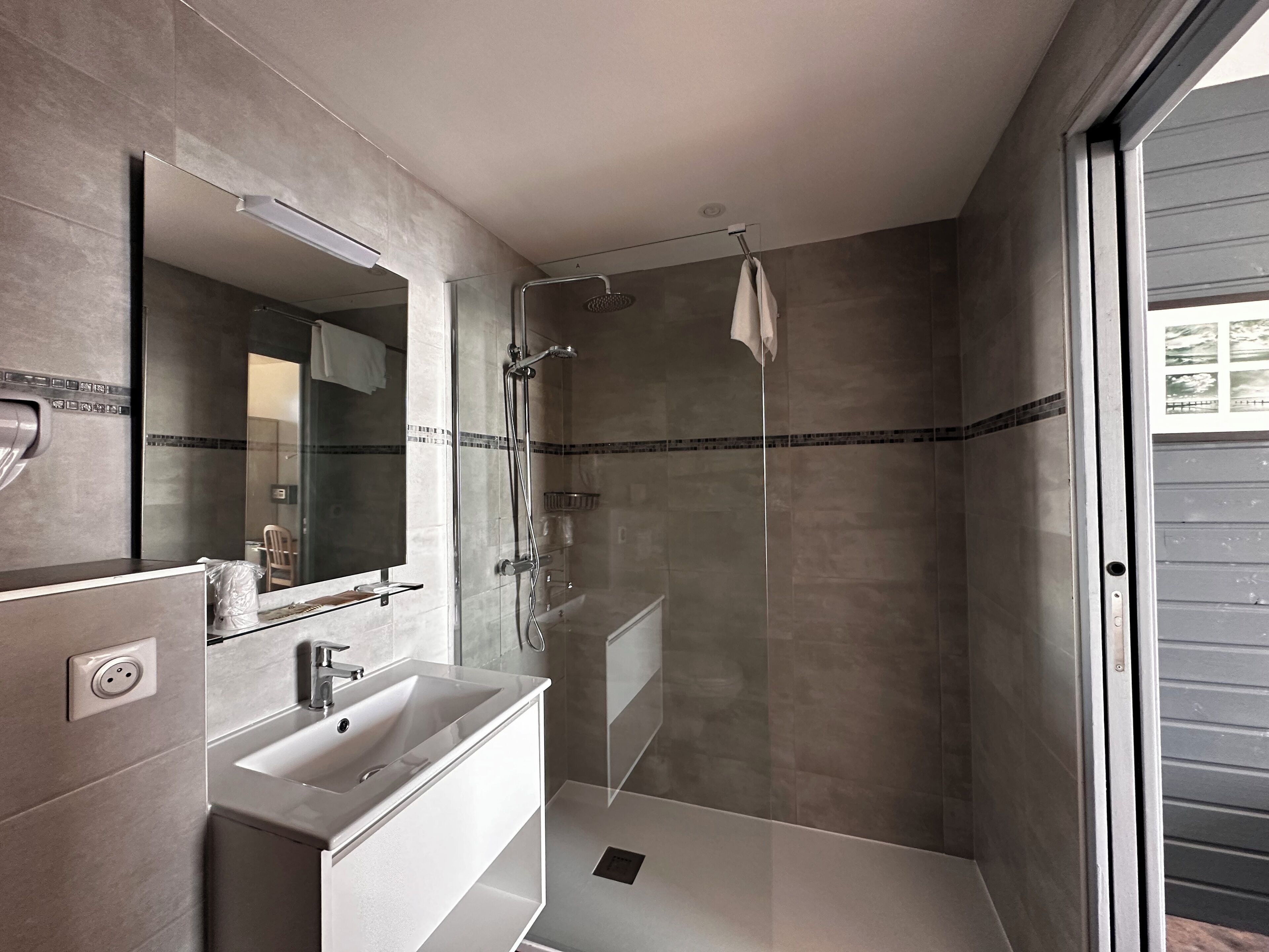 A modern bathroom with a glass-enclosed shower, a white sink, and a large mirror.