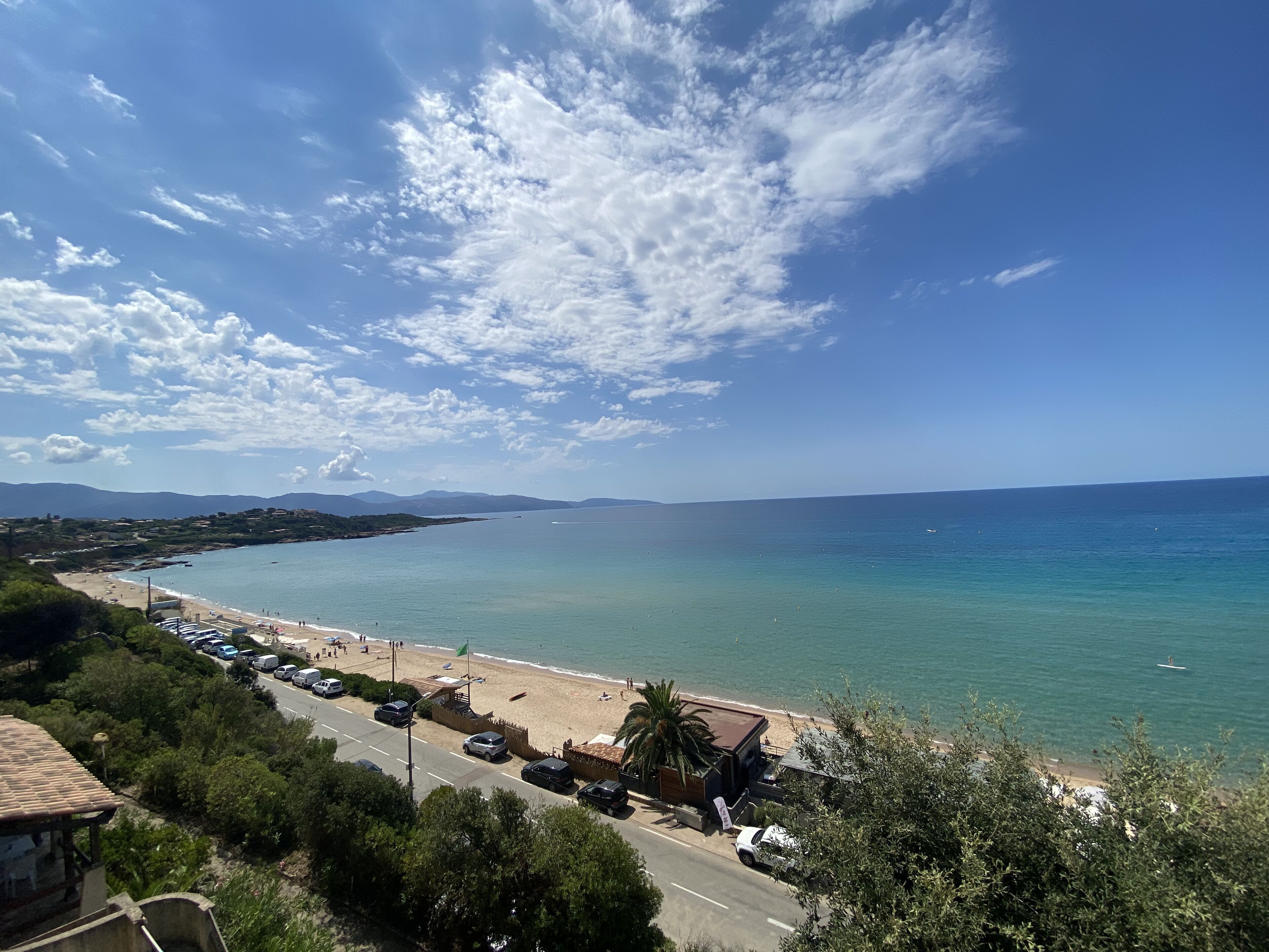 Une route côtière bordée de voitures garées, une plage et un ciel dégagé.