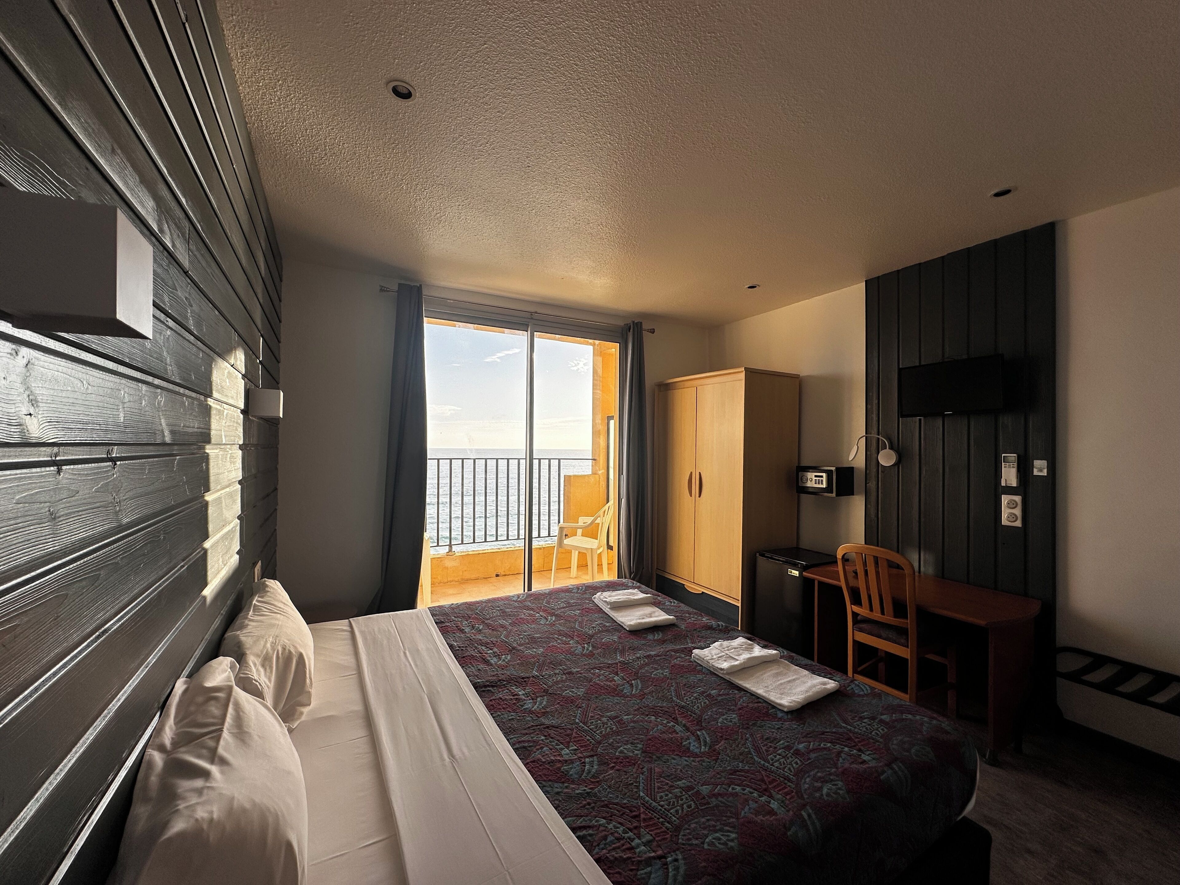 Habitación de hotel con cama, escritorio, silla, armario y televisor.