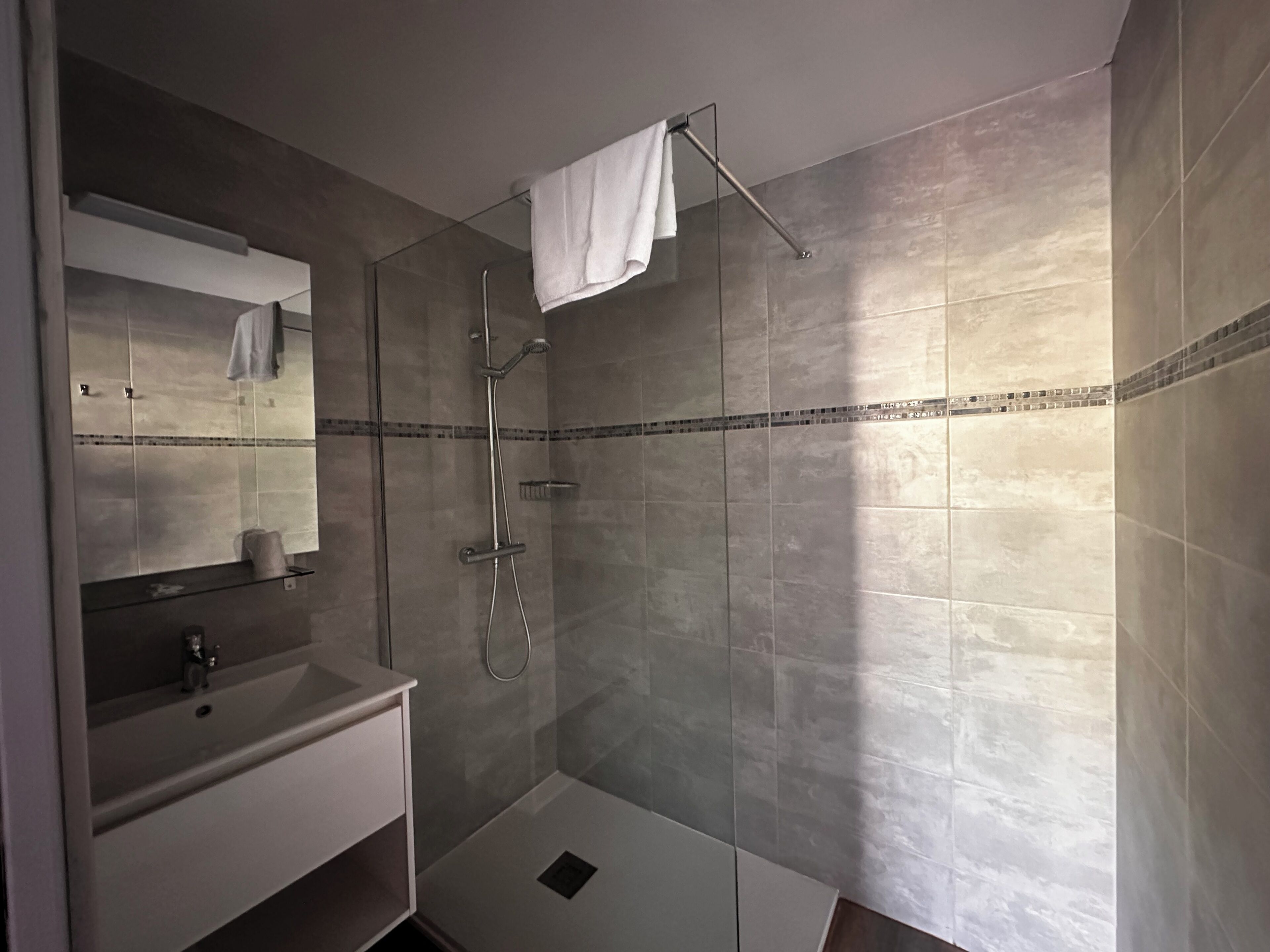 Un baño moderno con ducha de vidrio, tocador con espejo y toalla en un perchero.